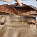 Close-up of a brown leather bag with a hand holding it open.