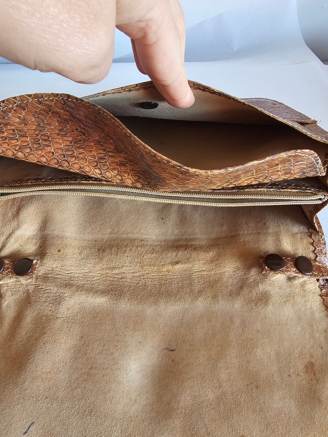 Close-up of a brown leather bag with a hand holding it open.