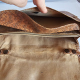 Close-up of a brown leather bag with a hand holding it open.