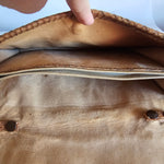 Close-up of a brown leather bag with a zipper, showing wear and tear.