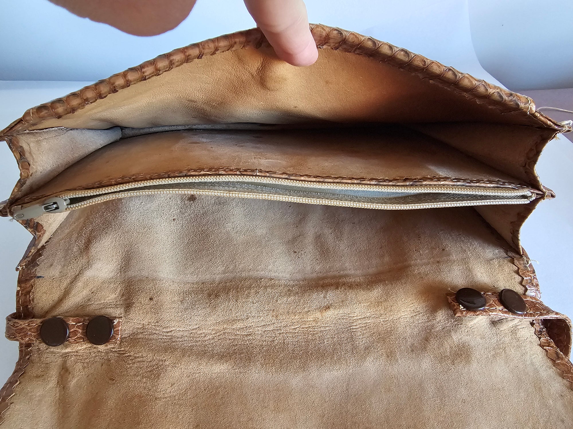 Close-up of a brown leather bag with a zipper, showing wear and tear.