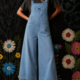 Person wearing a denim overalls with a floral and black patterned background