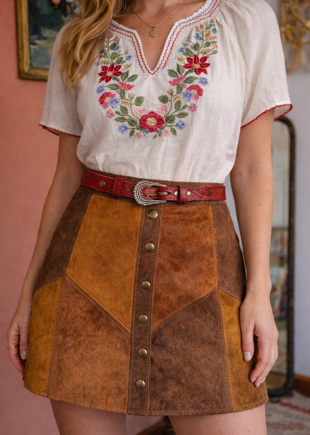 Woman wearing a white blouse with floral embroidery and a brown suede skirt.