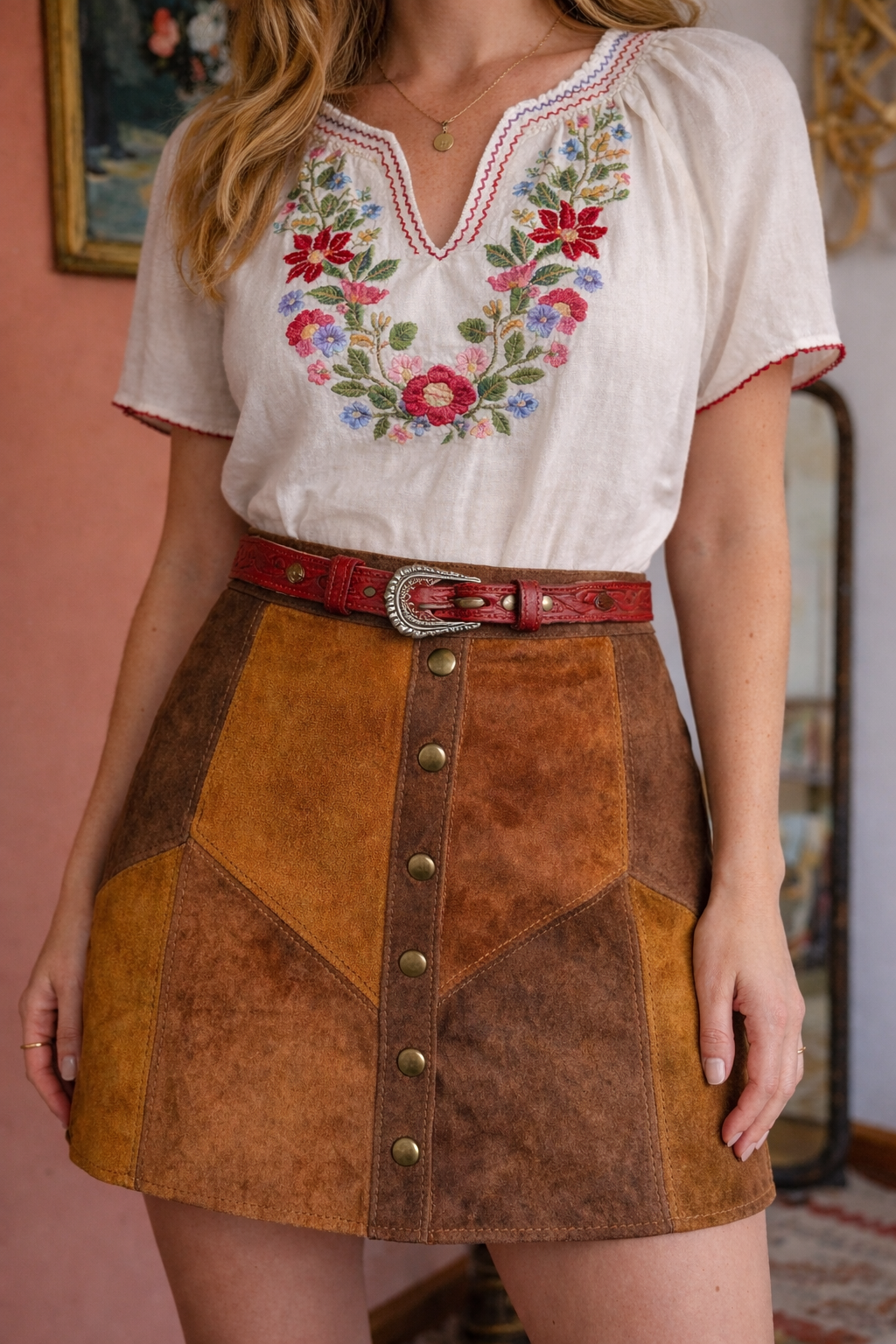 Woman wearing a white blouse with floral embroidery and a brown suede skirt.