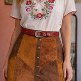Woman wearing a white blouse with floral embroidery and a brown suede skirt.