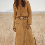Woman wearing a tan suede outfit with a belt and fringes in a desert landscape