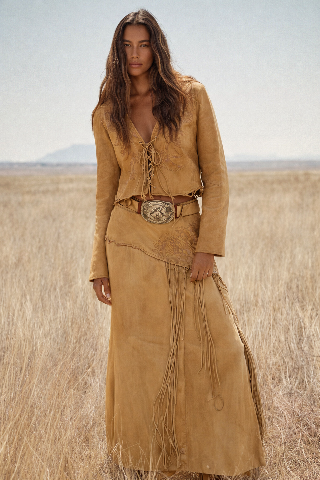 Woman wearing a tan suede outfit with a belt and fringes in a desert landscape
