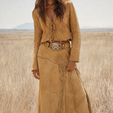 Woman wearing a tan suede outfit with a belt and fringes in a desert landscape