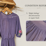 A lavender-purple midi dress with pink floral embroidery on the sleeves and hem, shown hanging on a wooden hanger against a light beige background. The image includes a 'Condition Reference' section with two inset close-ups highlighting fading on the upper back and front skirt, accompanied by explanatory text.