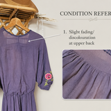 A lavender-purple midi dress with pink floral embroidery on the sleeves and hem, shown hanging on a wooden hanger against a light beige background. The image includes a 'Condition Reference' section with two inset close-ups highlighting fading on the upper back and front skirt, accompanied by explanatory text.
