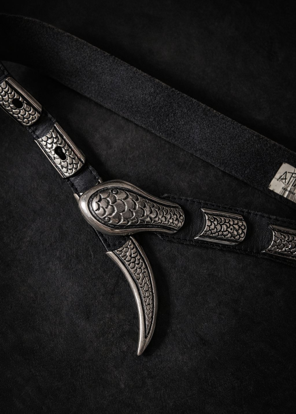 Close-up of a leather belt with decorative metal buckle on a dark background
