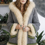 Woman wearing a gray coat with beige fur trim and a brown hat indoors. shearling penny lane coat