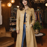 Woman wearing a beige coat in a clothing store with wooden walls and hanging lights.