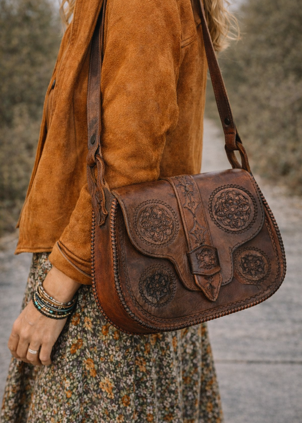 Person wearing a brown suede jacket and carrying a brown leather bag with intricate designs.