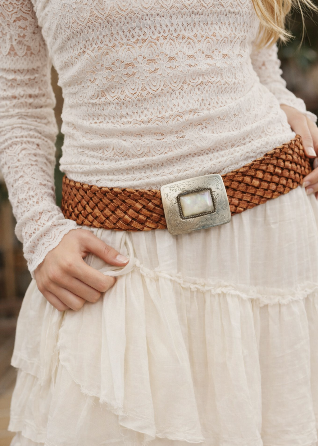Person wearing a white lace top and white ruffled skirt with a braided belt and silver buckle.