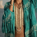 Woman wearing a teal fringe jacket with beads, beige top, and hat against a gray background