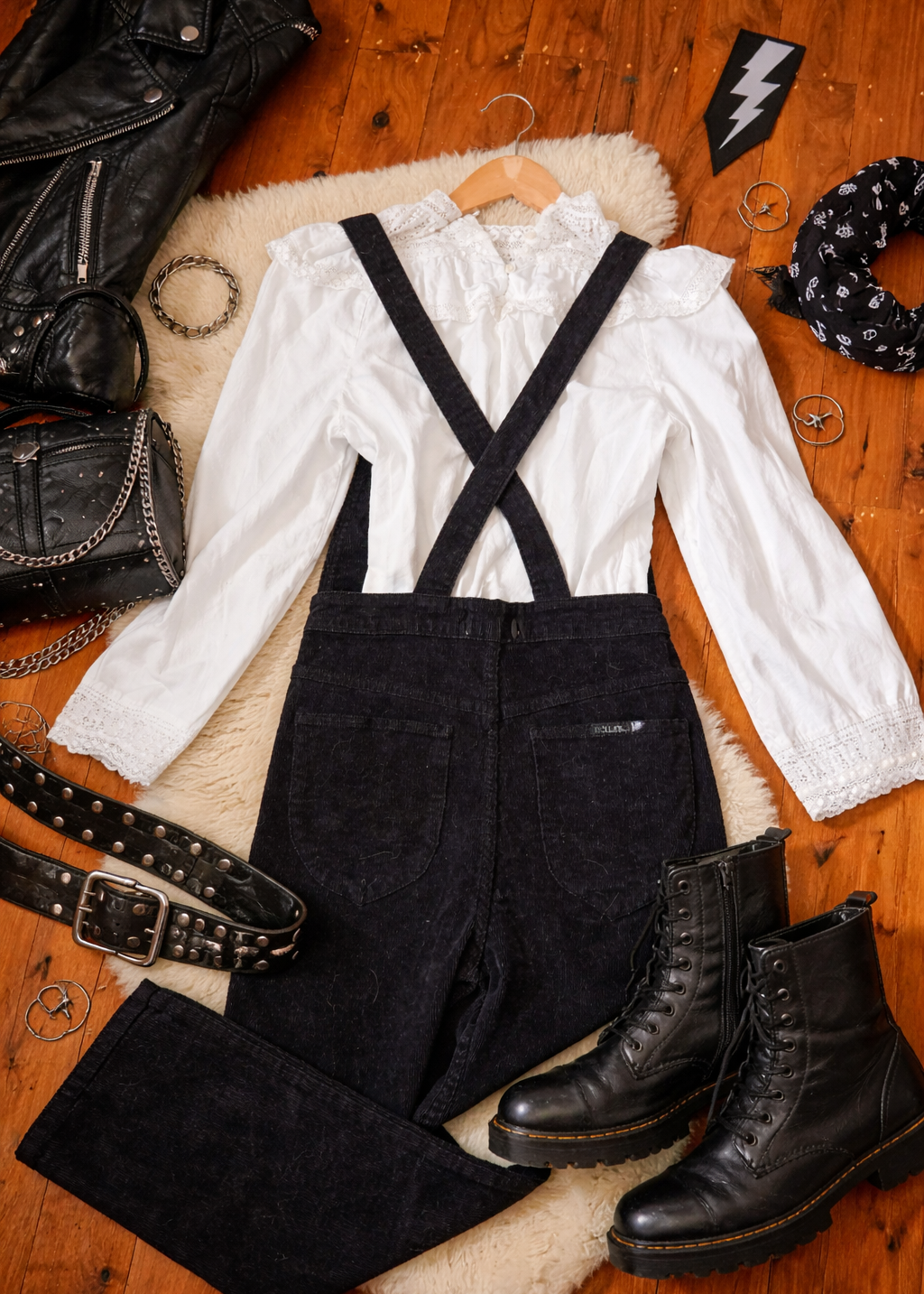 White blouse with black suspenders, black pants, and black boots on a wooden surface.