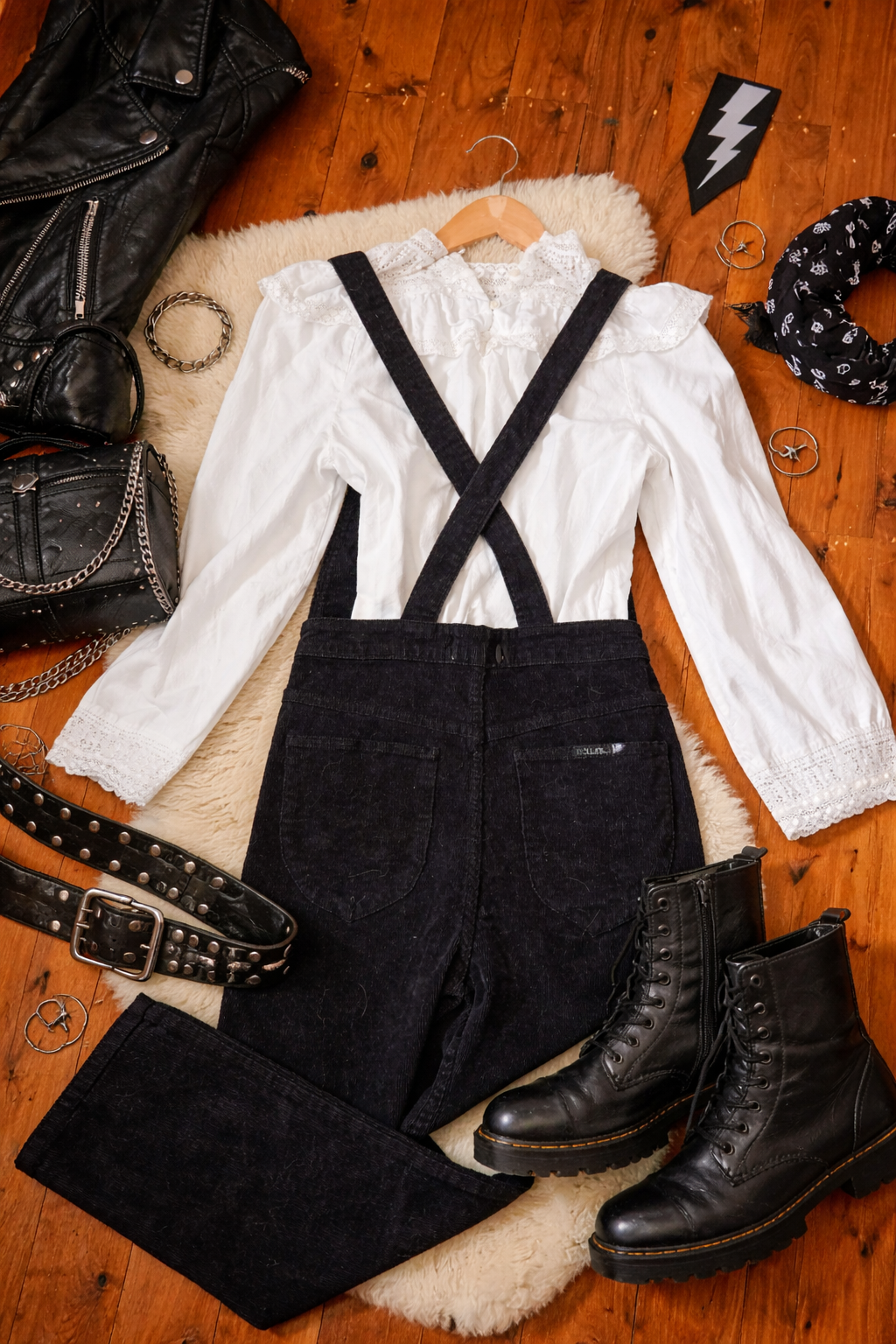 White blouse with black suspenders, black pants, and black boots on a wooden surface.