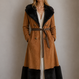 Woman wearing a long brown coat with black fur trim against a plain background