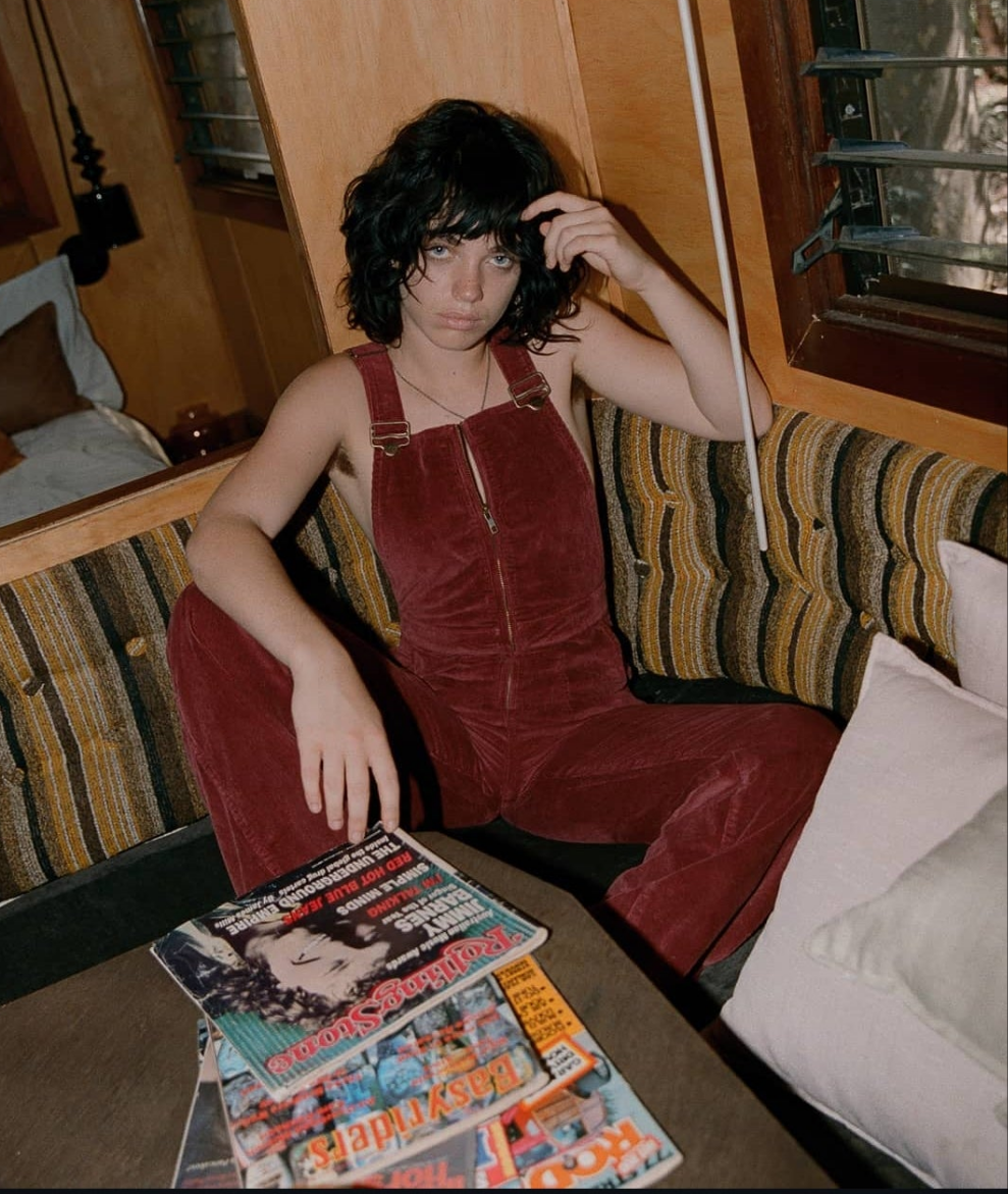 Person wearing red velvet overalls sitting on a couch with a magazine in front