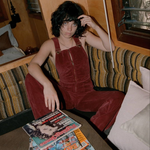 Person wearing red velvet overalls sitting on a couch with a magazine in front