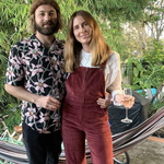 Two people standing together in a garden setting, holding drinks.