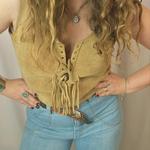 Person wearing a mustard yellow suede vest with fringes and blue jeans against a neutral background