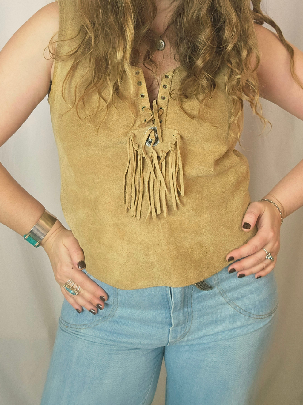 Person wearing a mustard yellow sleeveless top with fringe details and light blue jeans.