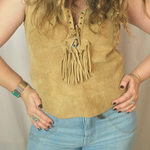 Person wearing a mustard yellow sleeveless top with fringe details and light blue jeans.