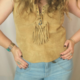 Person wearing a mustard yellow sleeveless top with fringe details and light blue jeans.