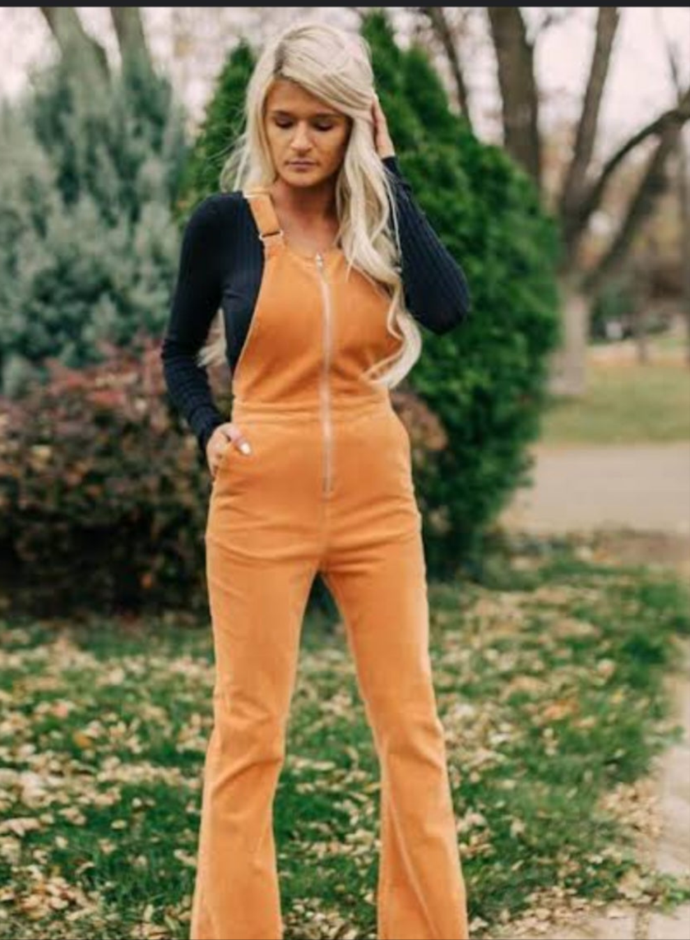 Woman wearing orange bell-bottom overalls and a dark jacket outdoors.