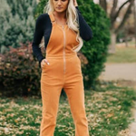 Woman wearing orange bell-bottom overalls and a dark jacket outdoors.