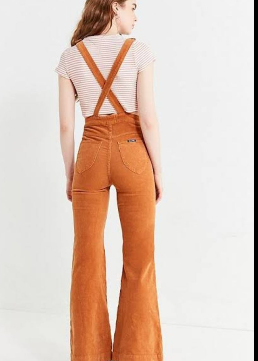 Person wearing brown corduroy overalls on a white background