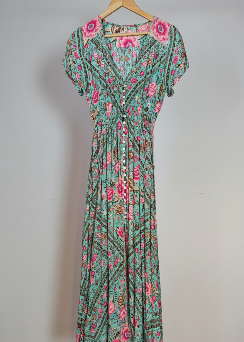 Floral dress with pink flowers on a hanger against a white wall.