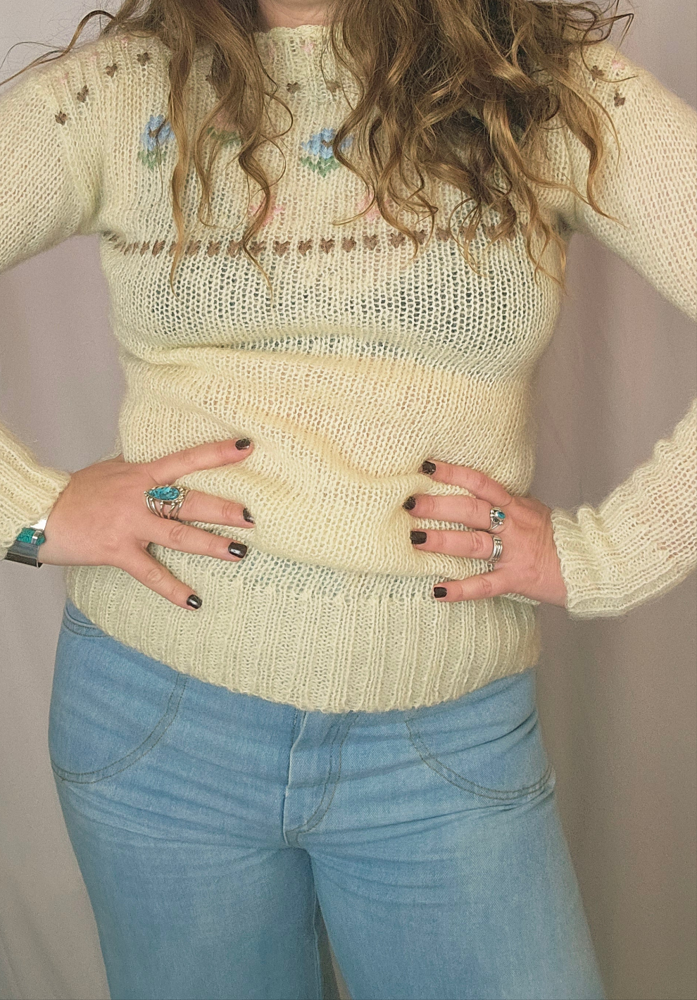 Person wearing a light-colored knitted sweater and blue jeans with a neutral background