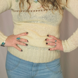 Person wearing a light-colored knitted sweater and blue jeans with a neutral background