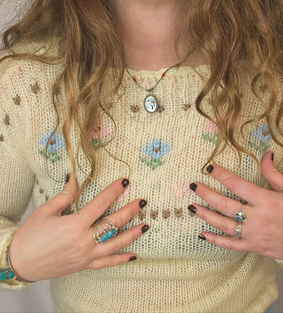 Person wearing a floral embroidered sweater with jewelry and nail polish.