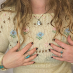 Person wearing a floral embroidered sweater with jewelry and nail polish.