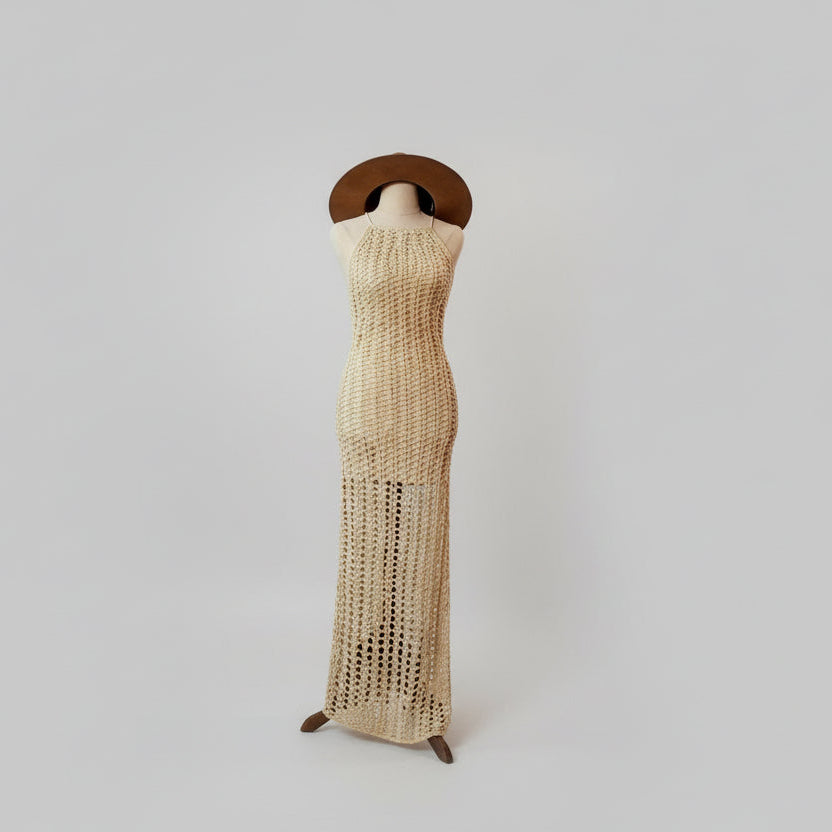 A crocheted beige mini dress with a low back and cross back detail, displayed on a mannequin with a wide-brimmed hat.