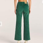 Green corduroy pants worn by a person on a light pink background