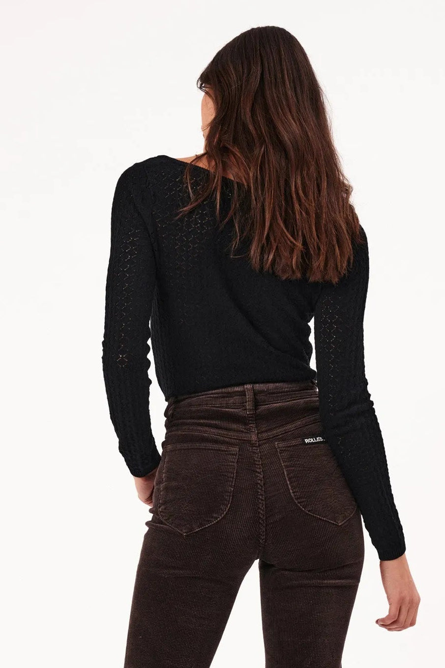 Person wearing brown flared jeans and a black top on a white background