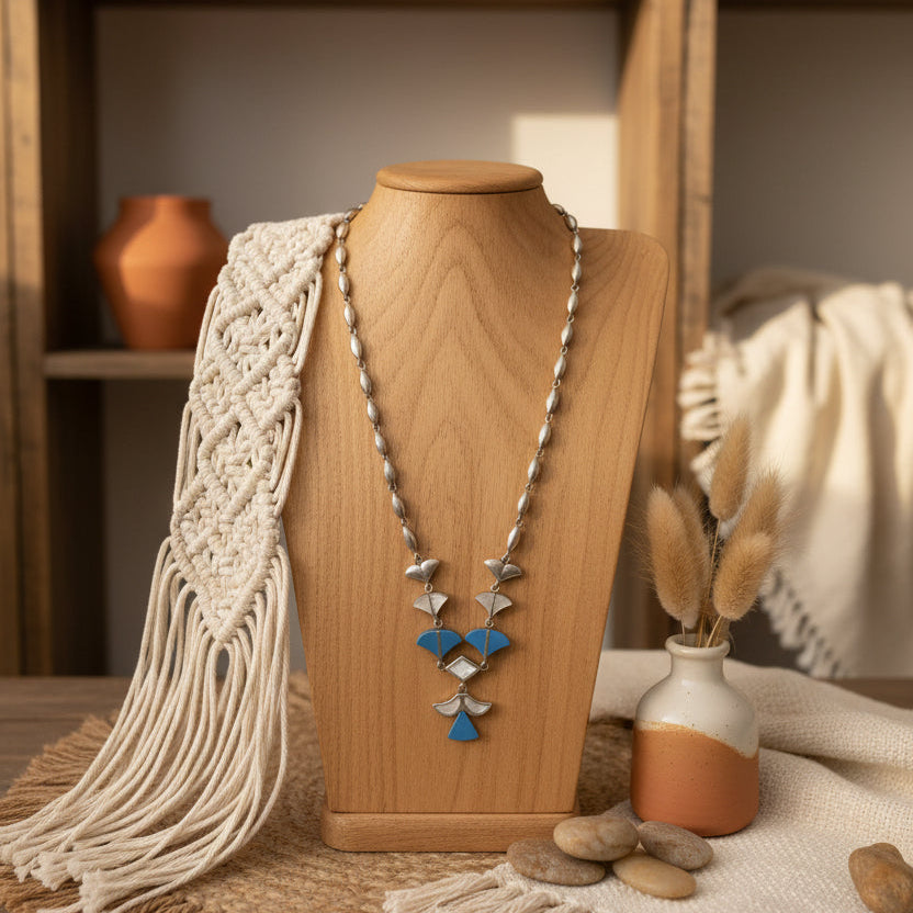 Necklace on a wooden mannequin with a macrame scarf and decorative vases in the background