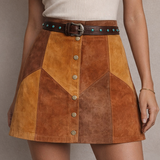 Person wearing a white top and brown patchwork skirt with buttons on a neutral background