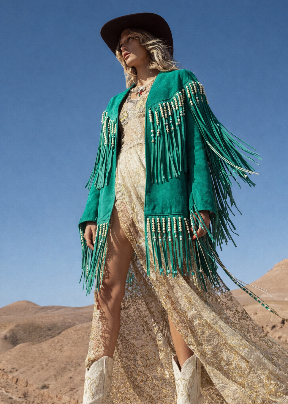 Woman in a green fringe jacket and white boots standing against a desert landscape