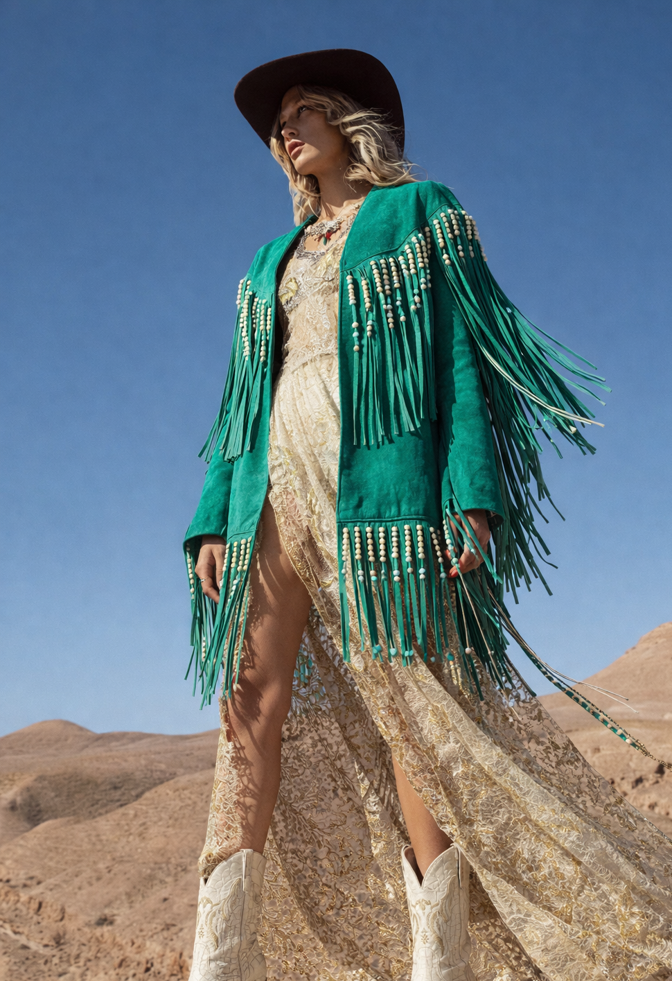 Woman in a green fringe jacket and white boots standing against a desert landscape