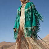 Woman in a green fringe jacket and white boots standing against a desert landscape