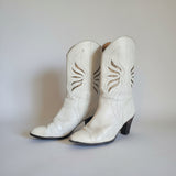 Pair of white leather boots with decorative stitching on a light background