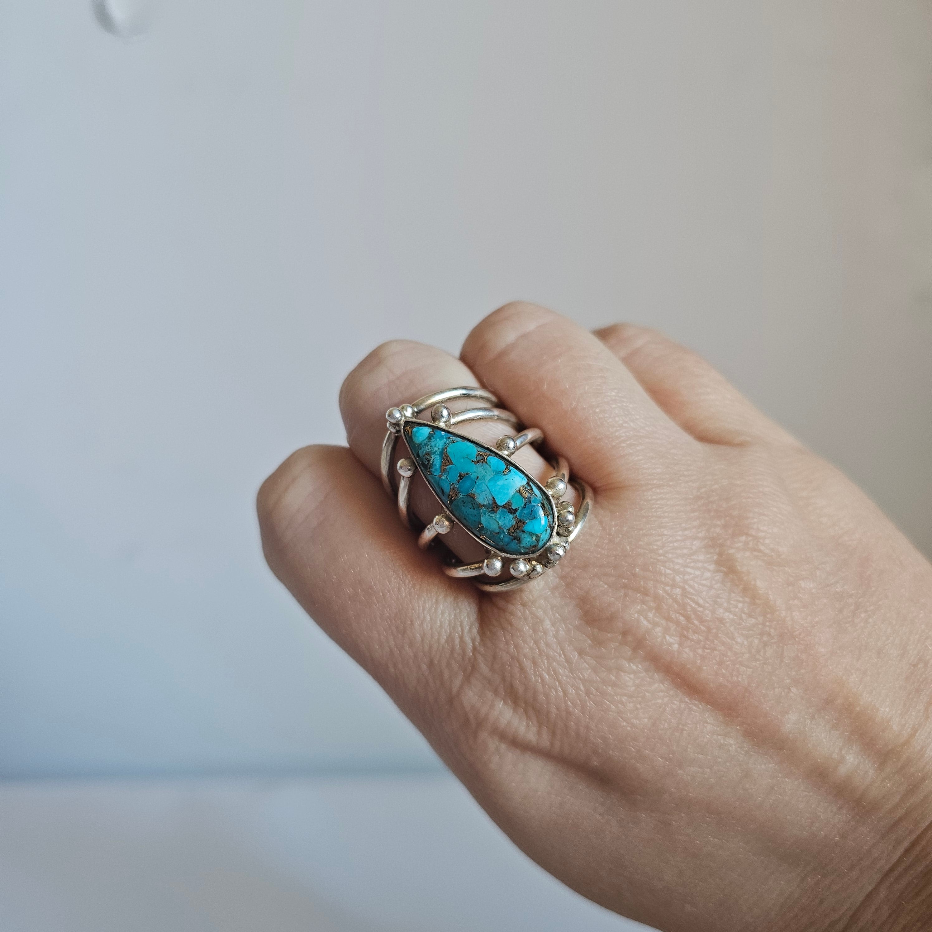 Hand wearing a ring with a turquoise stone on a neutral background
