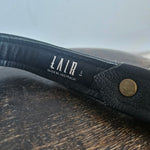 Black leather belt with a visible brand label on a wooden surface