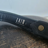 Black leather belt with a visible brand label on a wooden surface